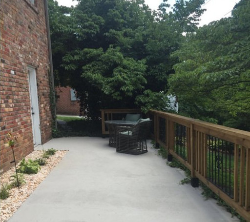 A freshly finished concrete porch with wood and iron railings, plant bed, and furniture